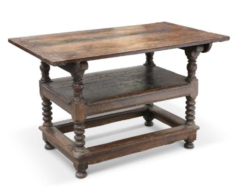 A 17TH CENTURY OAK MONKS BENCH the peg-hinged top raised on a block and baluster stand joined by a shelf and side stretchers 