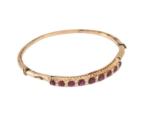 A RUBY AND DIAMOND BANGLE  The front section with nine graduated cushion cut rubies interspaced with pairs of old mine cut di