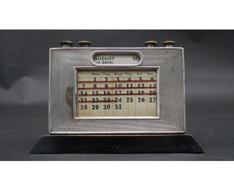 An antique ebonised wooden backed silver desk calendar with five knobs for adjusting month, day and date. Front has engine tu