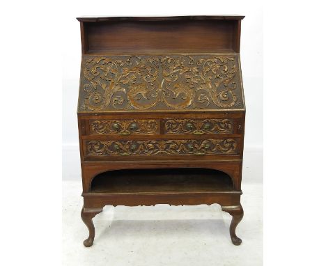 An ornately carved Edwardian oak bureau, with shelf rack over the drop flap, fitted two short drawers over one long drawer, w