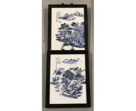 A pair of wooden framed Chinese ceramic plaques depicting Oriental mountainous scenes. In blue and white, with hand painted d