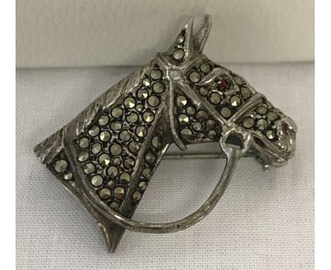 A vintage silver and marcasite brooch in the shape of a horses head with bridle. Horse's eye set with a small garnet. 