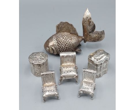 A group of three silver models in the form of chairs together with two silver pill boxes and a white metal model of a fish 