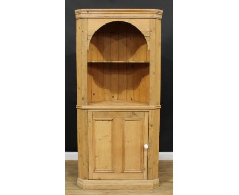 A pine floor-standing corner cabinet, arched open niche with shaped shelf above a panel door, skirted base, 192.5cm high, 92.