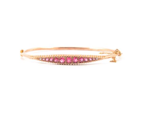 A 9 carat rose gold half hinged bangle set with eleven synthetic pink stones, graduating in size, width of bangle at front 6.