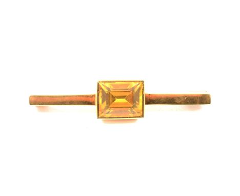 A yellow metal brooch set with a synthetic yellow sapphire, rectangular step cut stone, 12x9mm, rubbed over set to the centre