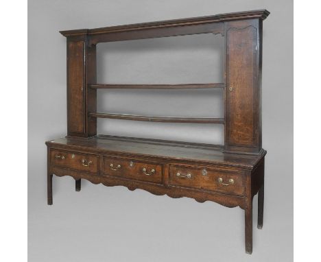 A GEORGE III OAK DRESSER, the top with a twin shelf plate rack flanked by long narrow cupboards, above a three drawer base on