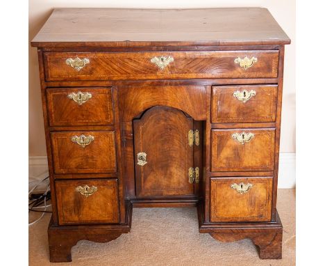 A George I walnut and feather-banded kneehole desk, circa 1720, the half-veneered top cross and feather banded above a frieze