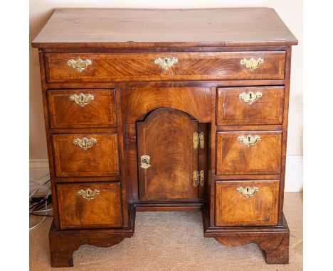 A George I walnut and feather-banded kneehole desk, circa 1720, the half-veneered top cross and feather banded above a frieze