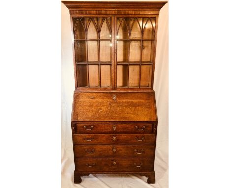 An early 19th Century late George III crossbanded oak glazed bookcase on bureau, circa 1820, moulded cornice above twin panel