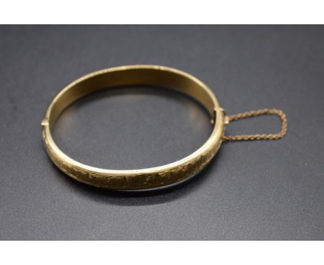 A 9ct gold shaped oval hinged bangle, by C &amp; F, Birmingham 1967,&nbsp;having chased floral decoration to one side,&nbsp;1