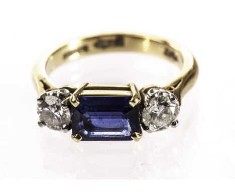 A modern three stone sapphire and diamond ring, having a rectangular cut blue stone in four claws and flanked by a brilliant 