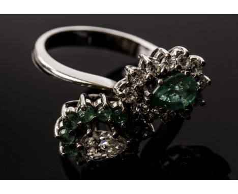 An impressive diamond and emerald crossover style dress ring, having a cluster of a pear shaped diamond surrounded by round c