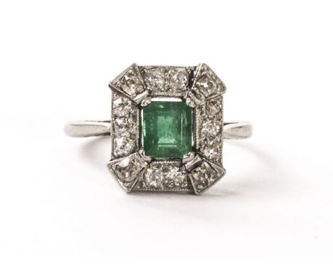 An Art Deco platinum diamond and emerald dress ring, of square form with canted lappet corners, having a square cut green sto