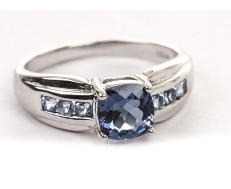 A modern 9ct gold and gem set dress ring, the white gold mount supporting a blue cushion cut stone set with three lighter blu