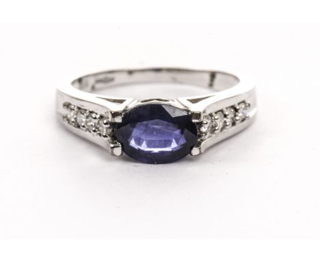 A modern 9ct gold and gem set ring, having an oval cut blue stone, possibly a sapphire, with four brilliant cuts to each shou