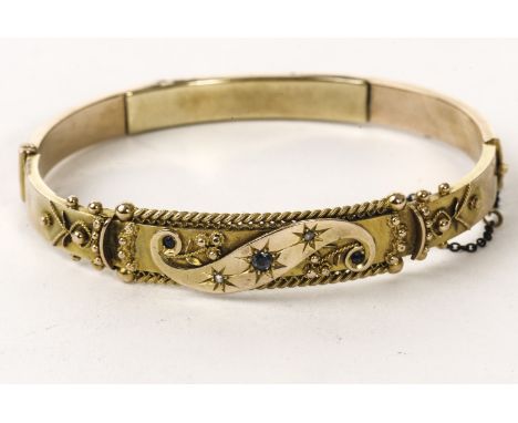 A 9ct gold and gem set bangle, the ornate tablet centred with a S scroll set with sapphires and diamonds, approx 10.8g