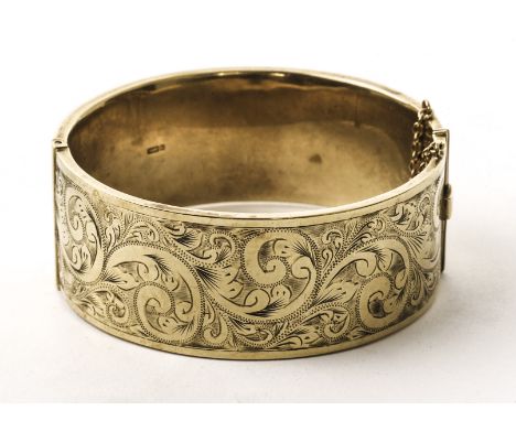 A 9ct gold bangle, the thick hinged bangle having one half with engraved scrolling foliage, the other half plain, hallmarked,