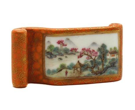 A Chinese famille rose ink rest,in the shape of a scroll, painted with a landscape in a rectangular panel, surrounded by prun