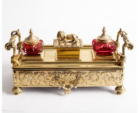 An engraved brass inkstand and pen tray, circa 1930, with Rococo style handles, fitted ink pots, sander and drawer beneath on