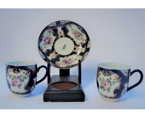 Two Worcester blue scale ground coffee cups and a saucer, circa 1770, painted flowers in gilt frame cartouches/Provenance: Fr