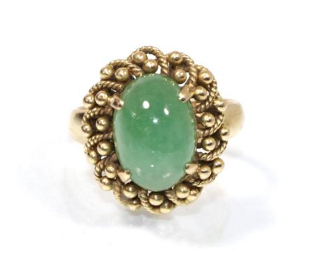 A cabochon jade ring in a beaded border, finger size J, stamped '14K', 6.4g