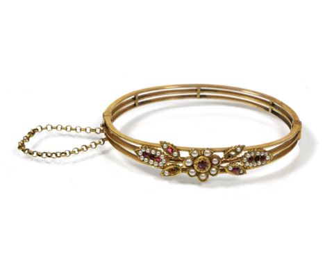 An early twentieth century ruby and pearl bangle, the front with a floral motif set with round cut rubies and seed pearls, to
