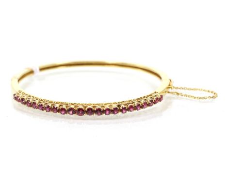 A ruby bangle, the front with graduated round cut rubies, to a plain hinged back, measures 4.8cm by 5.8cm inner diameter, sta