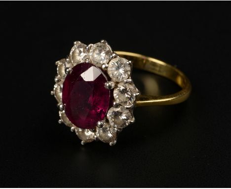 A RUBY AND DIAMOND CLUSTER RING, in 18ct yellow and white gold, the oval faceted ruby claw set and raised against a surround 