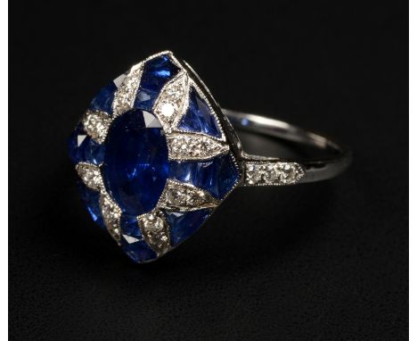 A SAPPHIRE AND DIAMOND CLUSTER RING, of Art Deco design, set to the centre with an oval faceted sapphire raised against a sur