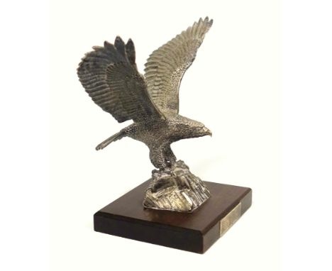 Silver model of an eagle naturalistically sculpted with its wings upstretched, perched on a rocky base, on a rectangular maho