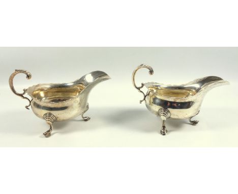 A pair of George V silver sauce boats in the 18th century taste, with wavy rims, leaf scroll handles on three shell capped sc