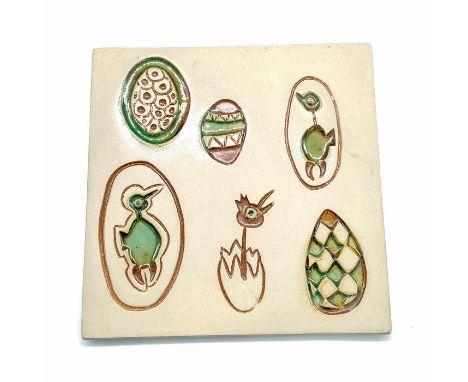 Ceramic tile with a green, blue, and yellow hand-painted glaze. Decorated with sunken reliefs of Easter eggs and chicks. Stam