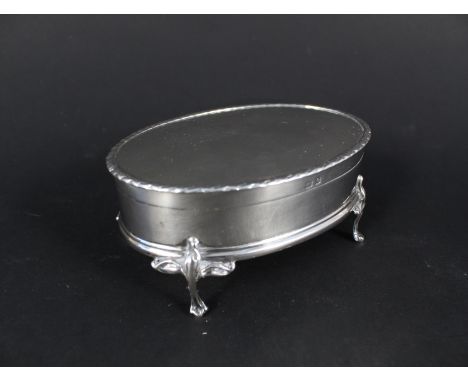 A silver ring box with gilt interior oval form with embossed border on four legs