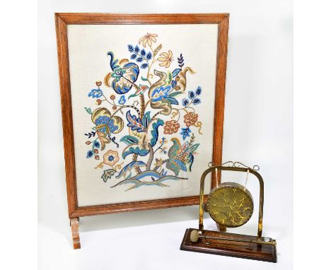 An early 20th century brass dinner gong on oak stand, together with an oak framed fire screen with tapestry panel (2).