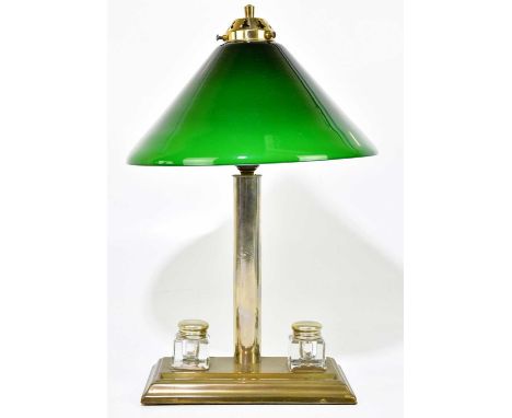 A brass plated desk lamp, the conical green glass shade on cylindrical column terminating on a plinth base with two detachabl