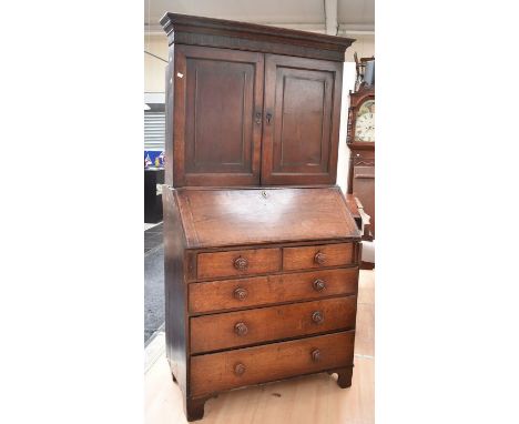 George III oak bureau/bookcase with panelled doors above a drop-down writing top. It has a quantity of small parcel drawers a