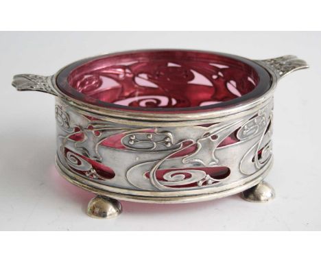 A Circa 1900 Art Nouveau silver circular twin handled table bowl, having a heavy ruby glass liner, with shaped and pierced st