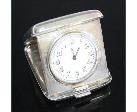 An Art Deco silver pocket travel clock, the engine turned hinged exterior enclosing hinged clock with white enamel dial, with