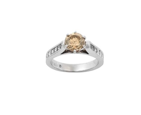 A Diamond Ringthe fancy cognac round brilliant cut diamond in a white claw setting, to tapered colourless princess cut diamon