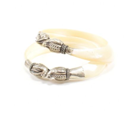 A pair of mother of pearl bangle bracelets. The bangles cared from a single shell having white metal stylized elephant finial