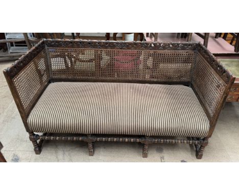 A three seater bergere settee with a scrolling carved rail, caned back and sides on bobbin turned legs with a pad seat, 152cm