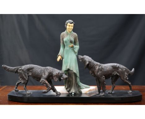 AN ART DECO-STYLE SPELTER AND IVORINE GROUP, depicting a lady in a green dress, flanked by a pair of dogs, to an angular marb