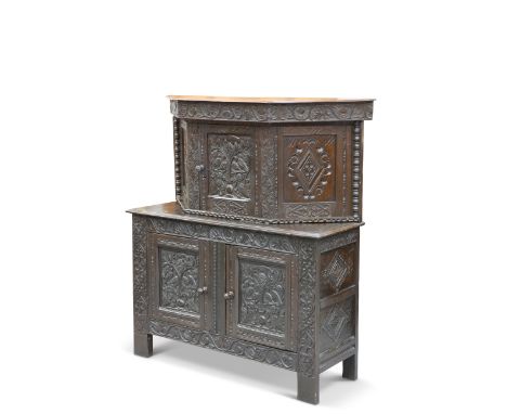 A CARVED OAK CUPBOARD, the canted upper section with a centre door and bobbin-turned pilasters, the base with a pair of cupbo