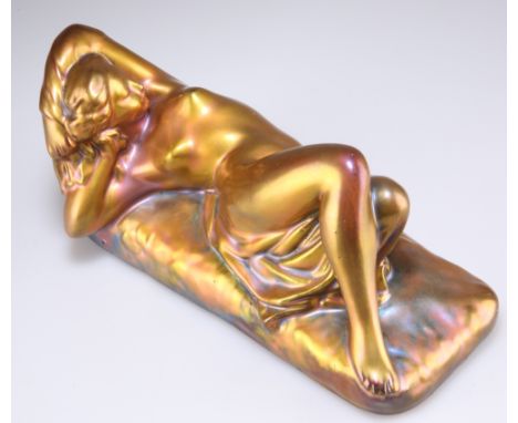 A ZSOLNAY PÉCS COPPER LUSTRE PORCELAIN MODEL OF A FEMALE NUDE, reclining on a rectangular base, printed marks, 8577.10.5cm by