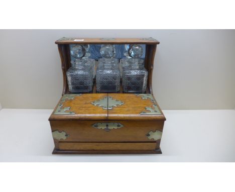 An oak three bottle games tantalus with a base card drawer - Height 33cm x 35cm x 27cm deep - small chips to all decanters, m