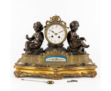 A mantle clock with two putti, patinated and gilt bronze with a Sèvres plaque.Standing a gilt wood pedestal.&nbsp;Circa 1900.