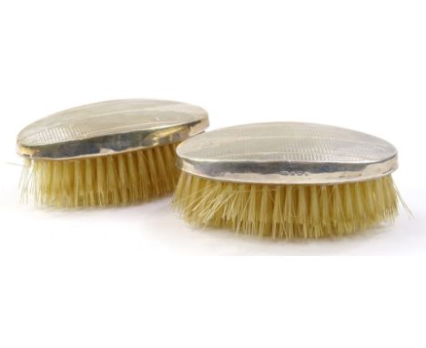 A pair of Art Deco design silver clothes brushes, of oval outline, partially engine turned, marks rubbed, 11cm wide. (2)