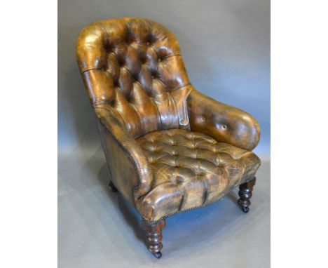 A Victorian Library Armchair with brown leather button upholstered back and seat raised upon turned legs 