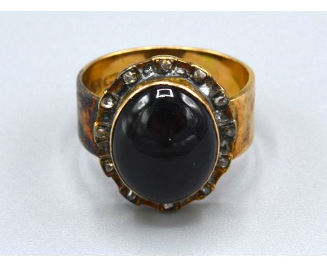 An 18ct. Gold Ring set with a cabochon oval garnet surrounded by diamonds, ring size K, 7.1 gms. 